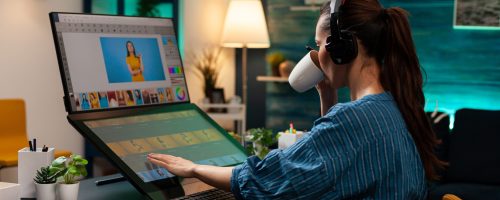 Woman with editor occupation wearing headphones at studio office desk. Professional graphic artist working on picture editing background for template using touchpad monitor screen